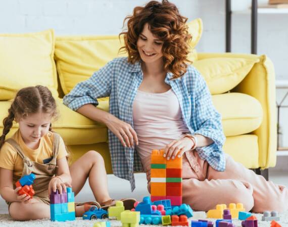 smiling nanny and adorable kid playing with multicolored building blocks on floor